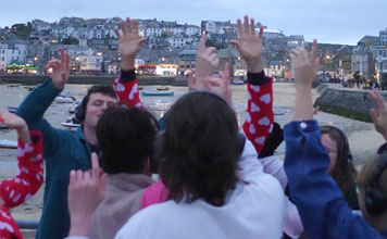 A group of people dancing wearing headphones with the town of ST Ives in the background